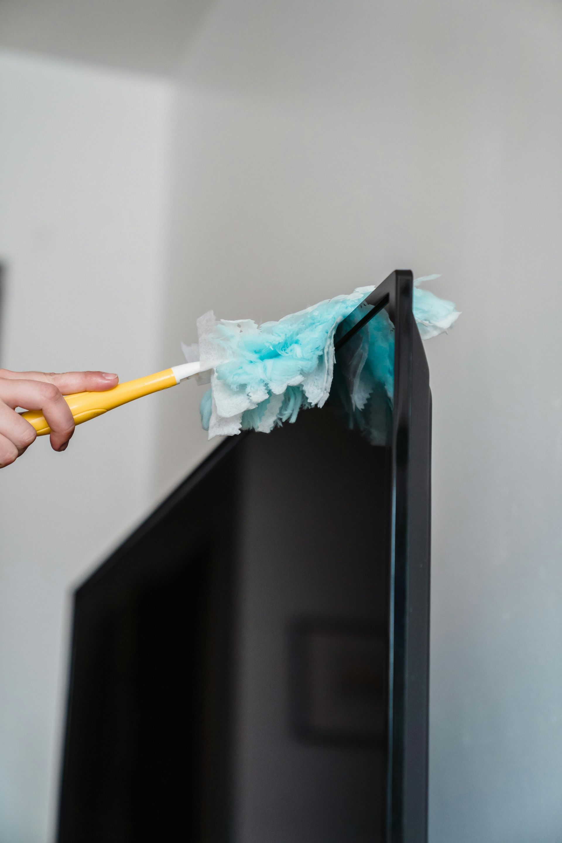 A close-up of cleaning a flat screen TV with a duster at home, showcasing housekeeping.
